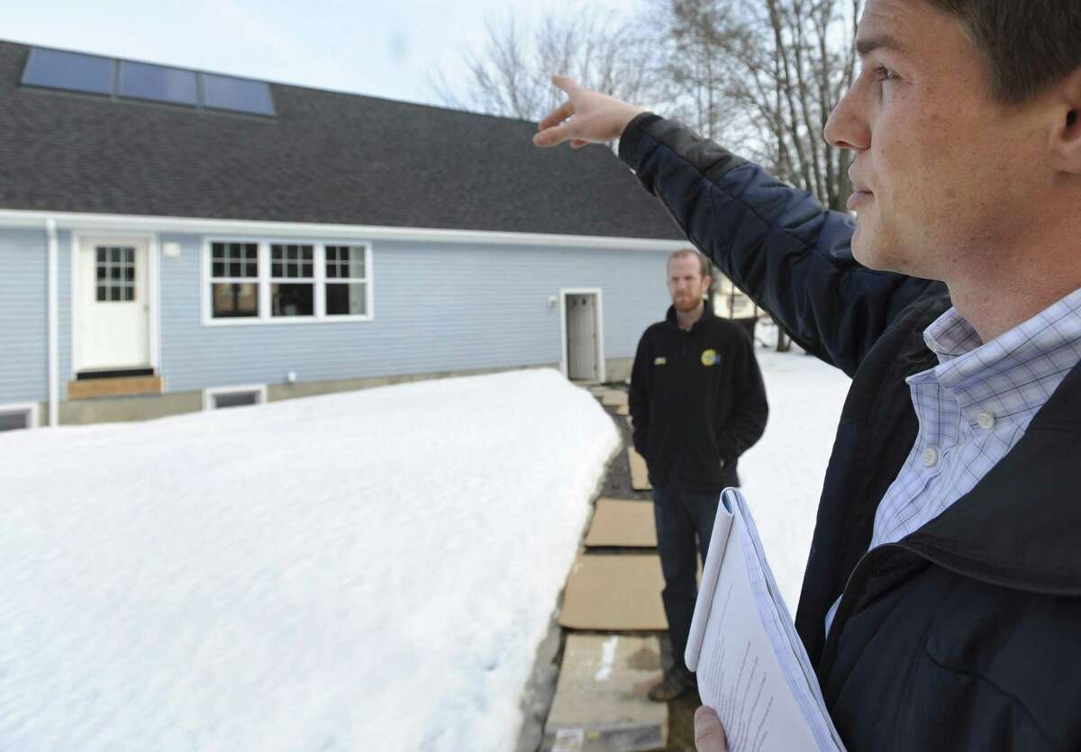 In this photo from Thursday, Tommy Cleveland, right, solar testing laboratory manager from the University of New Haven, gestures toward solar panels during a visit to Glen Mirmina's home as Joey Dorwart from Sunlight Solar Energy company, looks on, in Milford, Conn. The University of New Haven is expected to become an accredited testing lab for solar thermal products, reducing certification delays and boosting interest in solar thermal energy as an alternative to oil, natural gas and electricity. (AP Photo/Jessica Hill)
