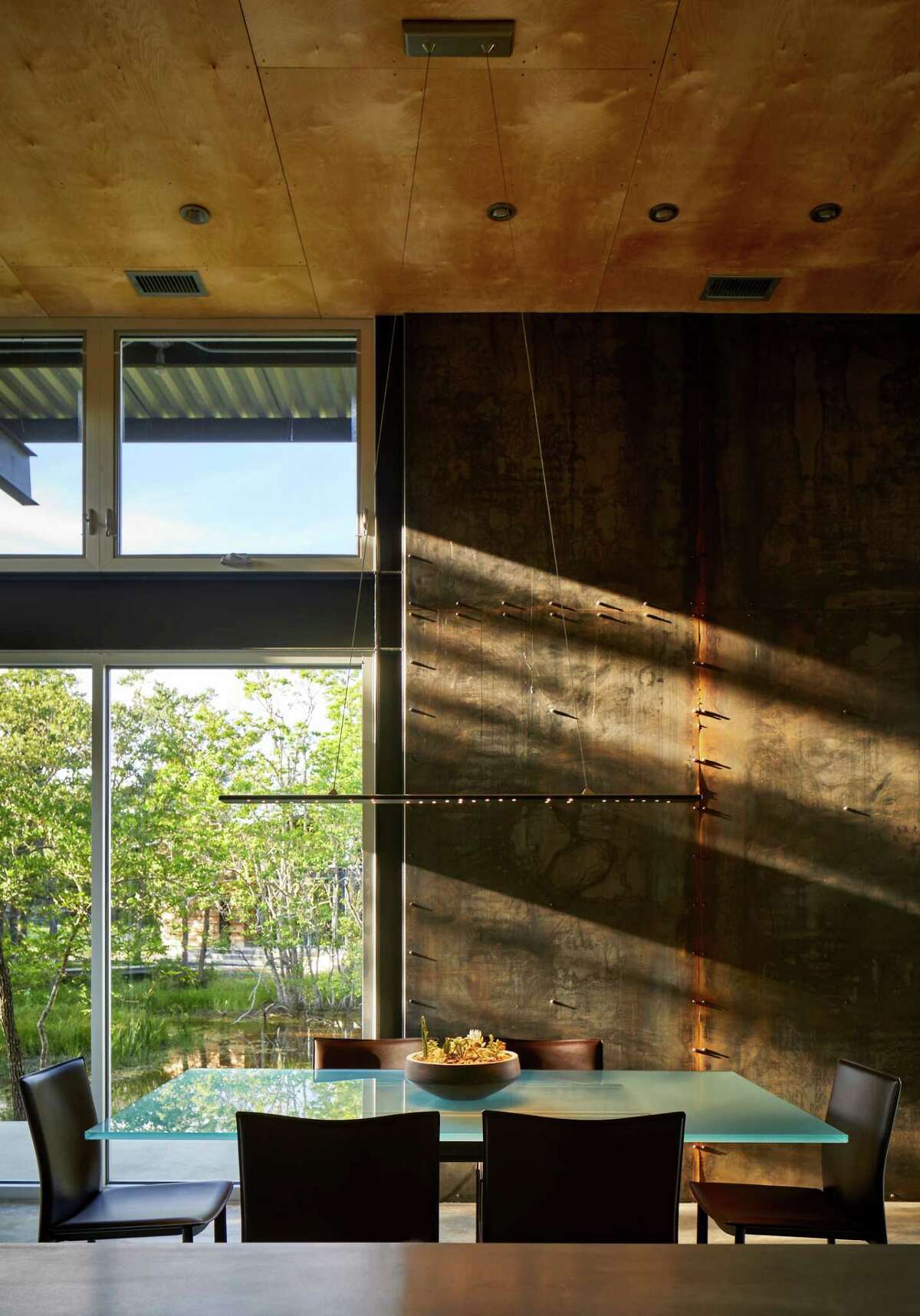 The dining room table is made of glass and Corten steel then surrounded by contemporary brown leather chairs.