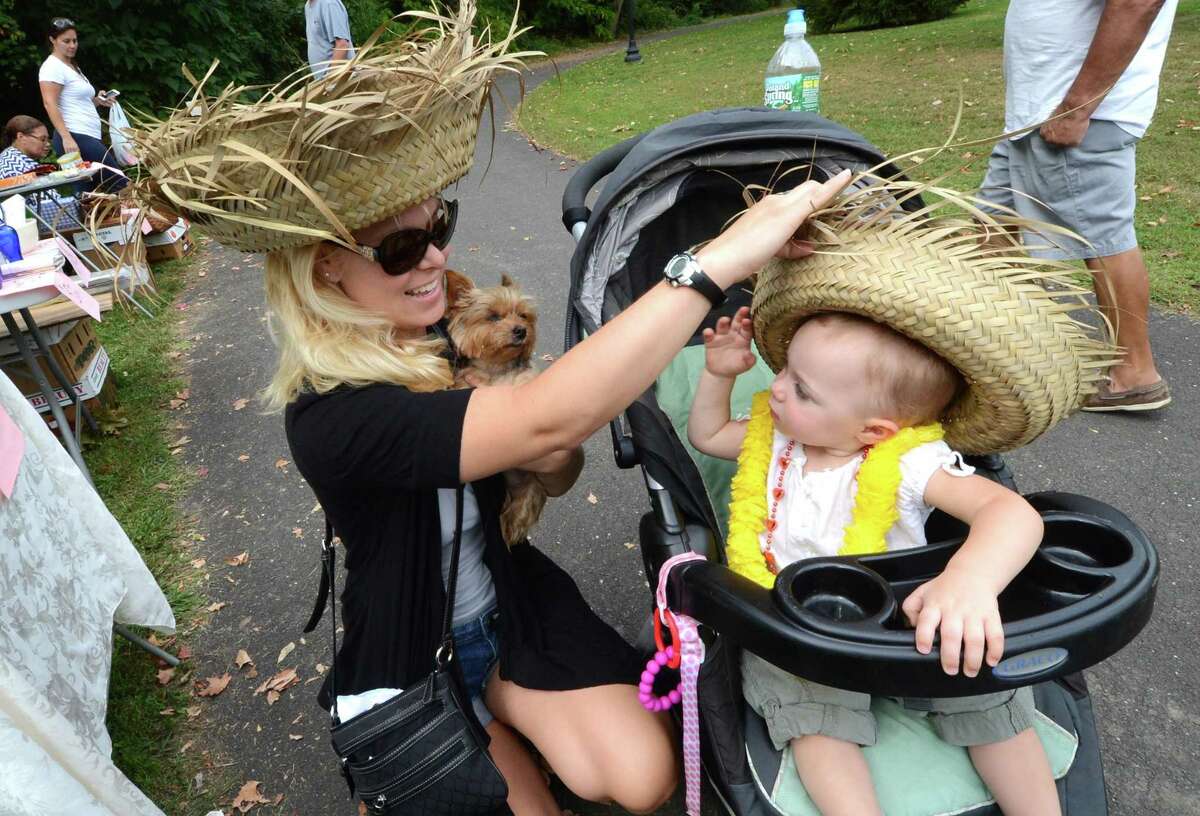 Jen Matsen from Norwalk trys to get a just bought straw hat on her 14-month-old daughter Courtney while holding her dog Kit Kat as they shop for unique items at the Lockwood-Mathews Mansion Museum Old-Fashioned Flea Market and antique car show in Norwalk.