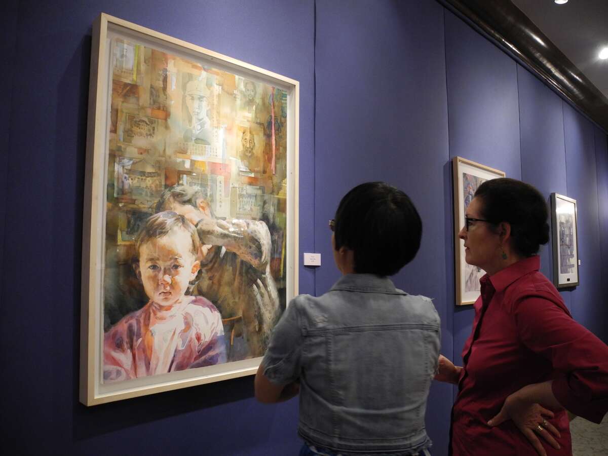 Dr. Yahui Zhang, associate professor of Communications and Media Studies, translates signs from Chinese in the watercolor painting “Haircut” by Stephen Zhang for Dr. Candace Keller at the Abraham Art Gallery.