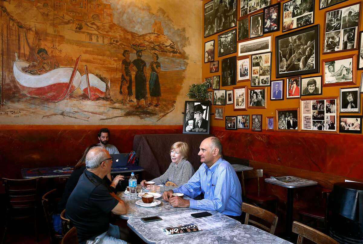 Patrons enjoy espresso drinks at Caffe Trieste below a mural and a wall of framed photos of famous previous guests of the North Beach institution, on Aug. 17, 2017.
