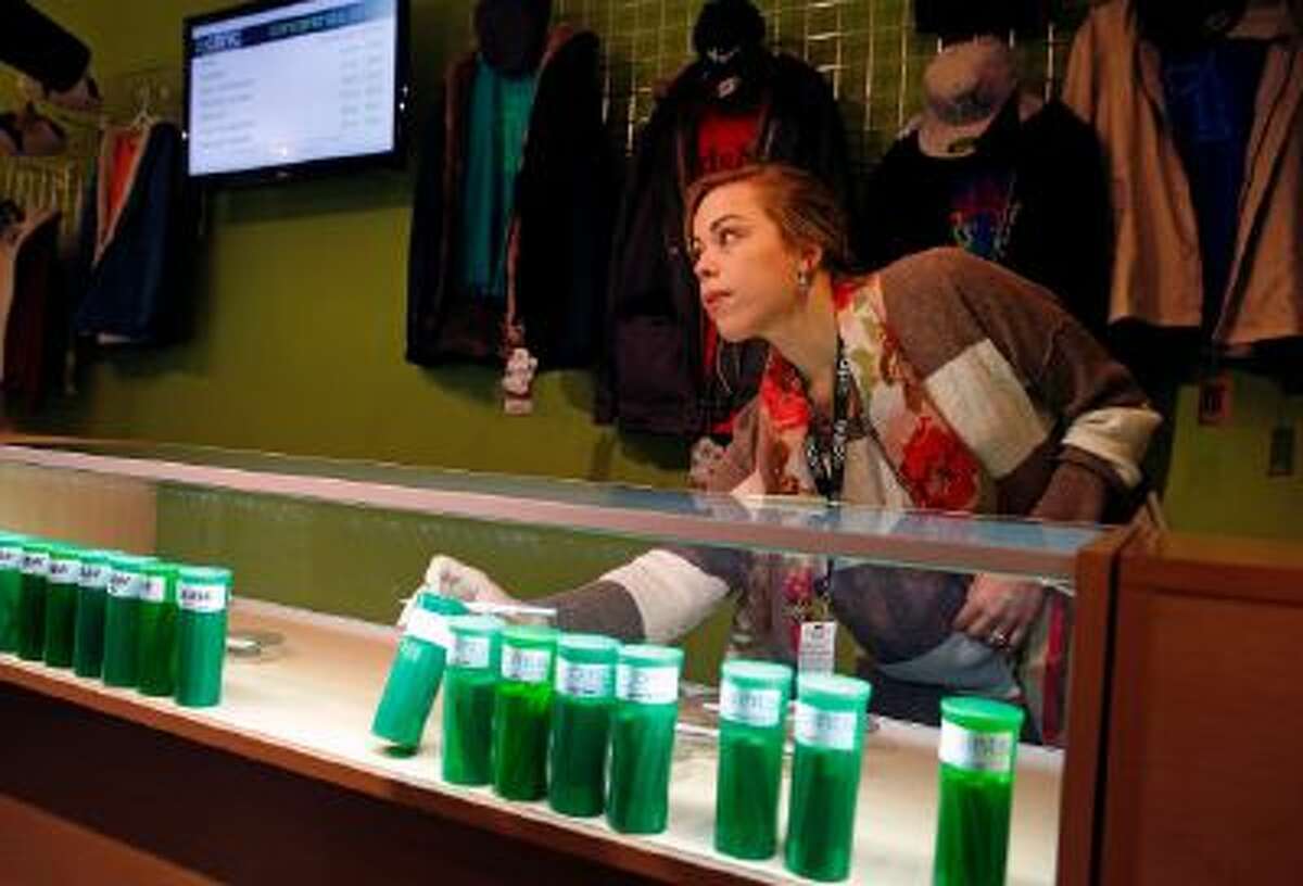 In this Dec. 6, 2013 photo, Elle Beau, an employee of The Clinic, a Denver-based dispensary with several outlets, reaches into a display case for marijuana while helping a customer, in Denver.