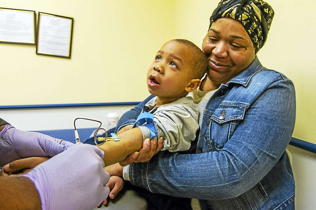 Three-year-old Kasheim Edwards is held by his mother as he looks up at the technician during a blood draw at the Connecticut Children's Primary Care Center in Hartford. His mother, Latasha Mewsom of Waterbury was alerted to elevated levels of lead in Kasheim's blood and now takes him to the center for continuing monitoring and treatment.  (Photo by Tony Bacewicz / C-Hit.org)