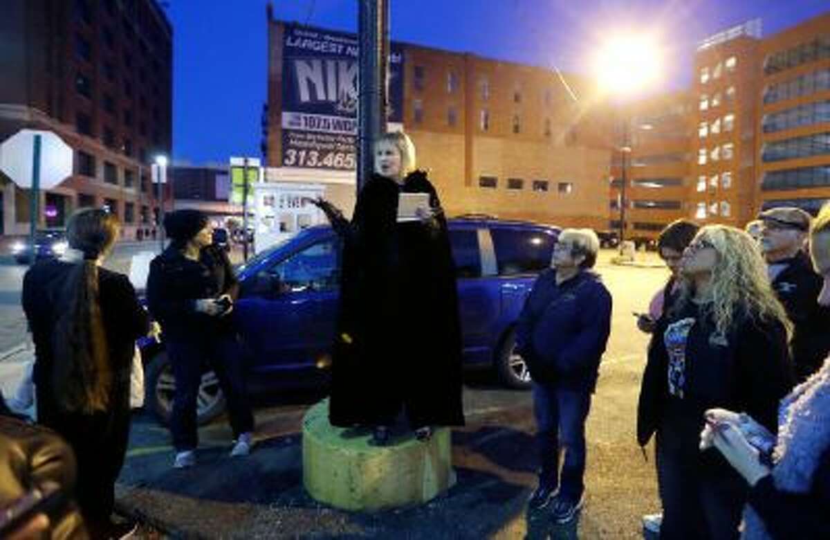 In this Friday, Oct. 18, 2013 photo, Karin Risko, center, tells a ghoulish tale on a Detroit street corner during the "Notorious 313 True Crime & Ghost Tour."