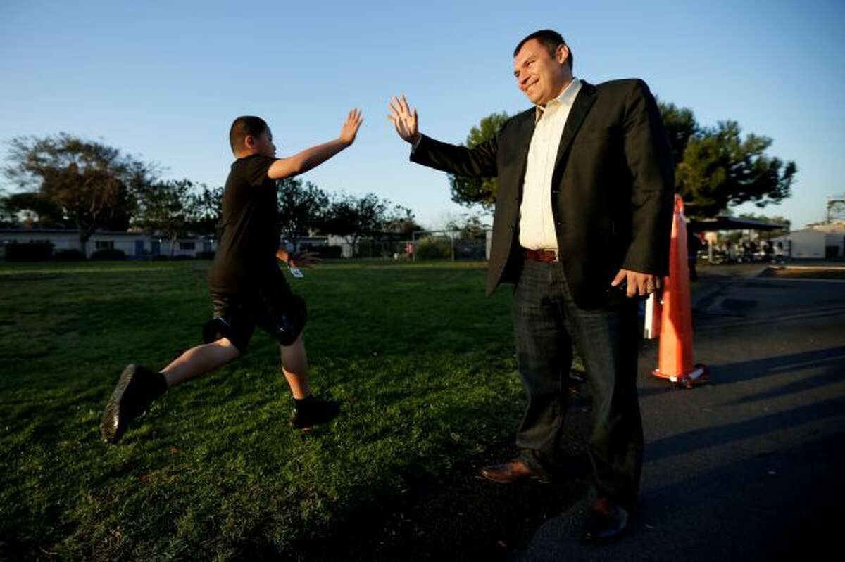 In this March 14, 2014 picture, Rice Elementary School Principal Ernesto Villanueva slaps hands with students during an early morning running program at an elementary school in Chula Vista, Calif. Amid alarming national statistics showing an epidemic in childhood obesity, hundreds of thousands of students across the country are being weighed and measured. Beltran son's Chula Vista Elementary School District is being touted as a model for its methods that have resulted in motivating the...