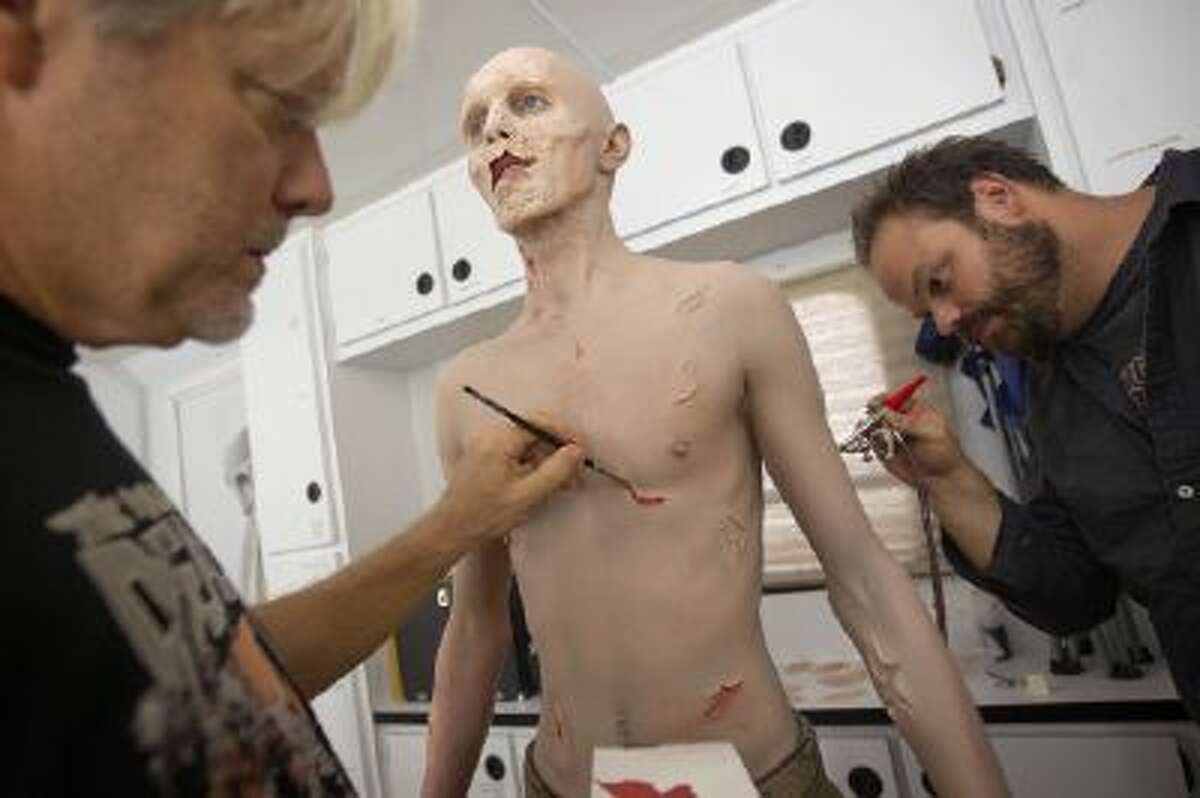 In this photo taken Friday, Oct 7, 2012, Kevin Galbraith, 24 of Marietta, Ga., undergoes a three hour make-up session to transform into his zombie character with the help of effects make-up artists Andy Schoneberg, right, and Kevin Wasner, left, on the set of AMC's television show, ?The Walking Dead,? in Senoia, Ga.