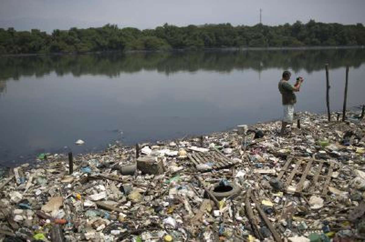 In this Oct. 23, 2013 photo, biologist Mario Moscatelli takes photographs from trash floating on the polluted waters of the Canal do Fundao in Rio de Janeiro, Brazil. Moscatelli, who oversees the reforestation of mangrove forests along the bay, said he fears that even if the bay is cleaned up, the state will let it deteriorate after all the athletes have gone home