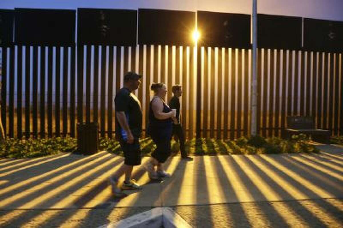In this Nov. 15, 2013 photo, Tijuana-based tour guide Derrik Chinn, right, leads Michael Beverly and his wife Amanda, both of Newfoundland, Canada, on an evening walk along the Mexican side of the border as floodlights beam through the border structure from the United States side, in Tijuana, Mexico.