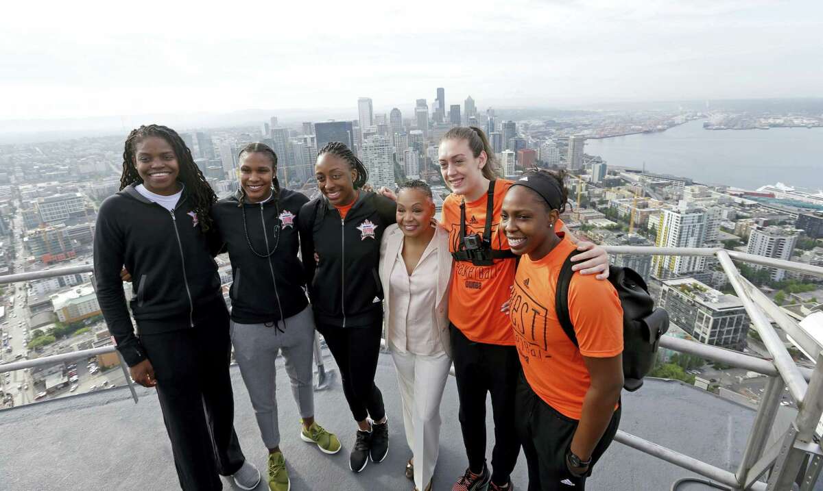 WNBA basketball All-Star players Connecticut Sun’s Jonquel Jones, left, Minnesota Lynx’s Rebekkah Brunson, Los Angeles Sparks’ Nneka Ogwumike, WNBA president Lisa Borders, Seattle Storm’s Breanna Stewart and Sparks’ Chelsea Gray stand on a platform in view of downtown Seattle and Elliott Bay about 575-feet high atop the Space Needle after raising the league flag atop the structure Friday. The WNBA All-Star game is Saturday in Seattle.