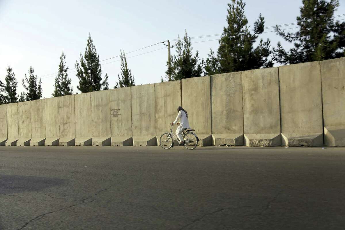 In this Monday, July 31, 2017, photo, an Afghan man rides his bicycle walks past blast walls in Kabul, Afghanistan. A U.S. watchdog says unprecedented security restrictions are making it difficult to monitor Afghanistan projects that are costing hundreds of millions of U.S. tax dollars. Despite tight security, an explosion inside a minority Shiite mosque in western Herat, on the border with Iran, has killed at least 20 people.