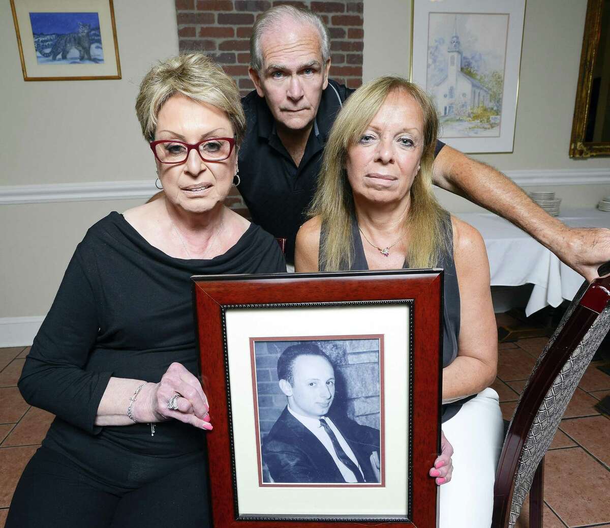 Toni Lupinacci, Fran Gross, and brother-in-law, Anthony "Butch" Lupinacci are photograph on August 23, 2017 with a portrait of Joe Pellicci at the family's restaurant on Stamford's Westside. Pellicci, shown in a portrait photograph taken around 1961 that hangs in the entrance way of Pellicci's Restaurant, was killed in 1973 in one of Stamford's most notorious murders, that remains still unsolved. They hope a soon-to-be-made TV show about the cold case prompts Stamford police to reopen it.