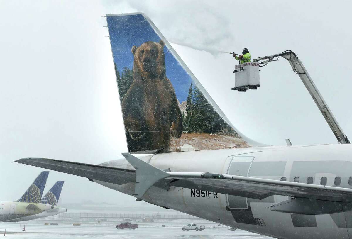 A crewmember de-ices a Frontier Airlines plane at LaGuardia Airport in New York, Monday, Jan. 26, 2015. More than 5,000 flights in and out of East Coast airports have been canceled as a major snowstorm packing up to three feet of snow barrels down on the region.