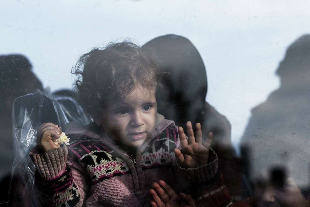In this Nov. 27, 2014 photo, a baby looks out from the window of a bus after disembarking from a crippled freighter carrying hundreds of refugees trying to migrate to Europe, at the coastal Cretan port of Ierapetra, Greece.