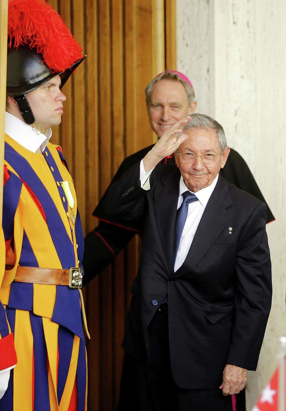 Cuban President Raul Castro waves as a Swiss Guard, left, and Archbishop George Gaenswein stand by him, prior to meeting Pope Francis, at the Vatican, Sunday, May 10, 2015. Cuban President Raul Castro received a warm welcome at the Vatican Sunday from Pope Francis, who played a key role in the breakthrough between Washington and Havana aimed at restoring U.S.-Cuban diplomatic ties, and later lavished praise on the pontiff for his "wisdom." (Fabio Frustaci/ANSA via AP)