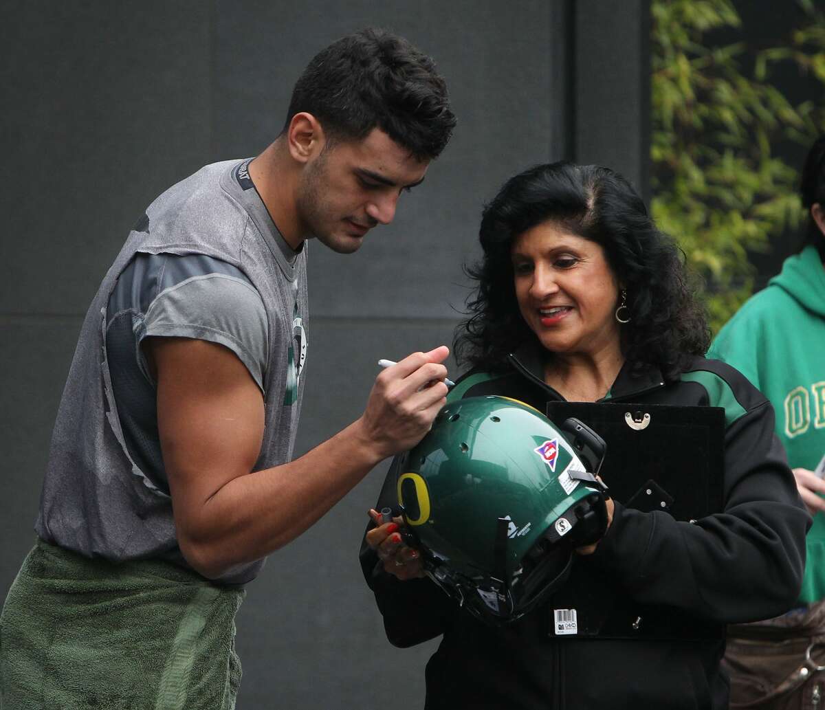 Oregon quarterback Marcus Mariota, left, signs an autograph for a fan after Wednesday’s practice in Eugene, Ore.