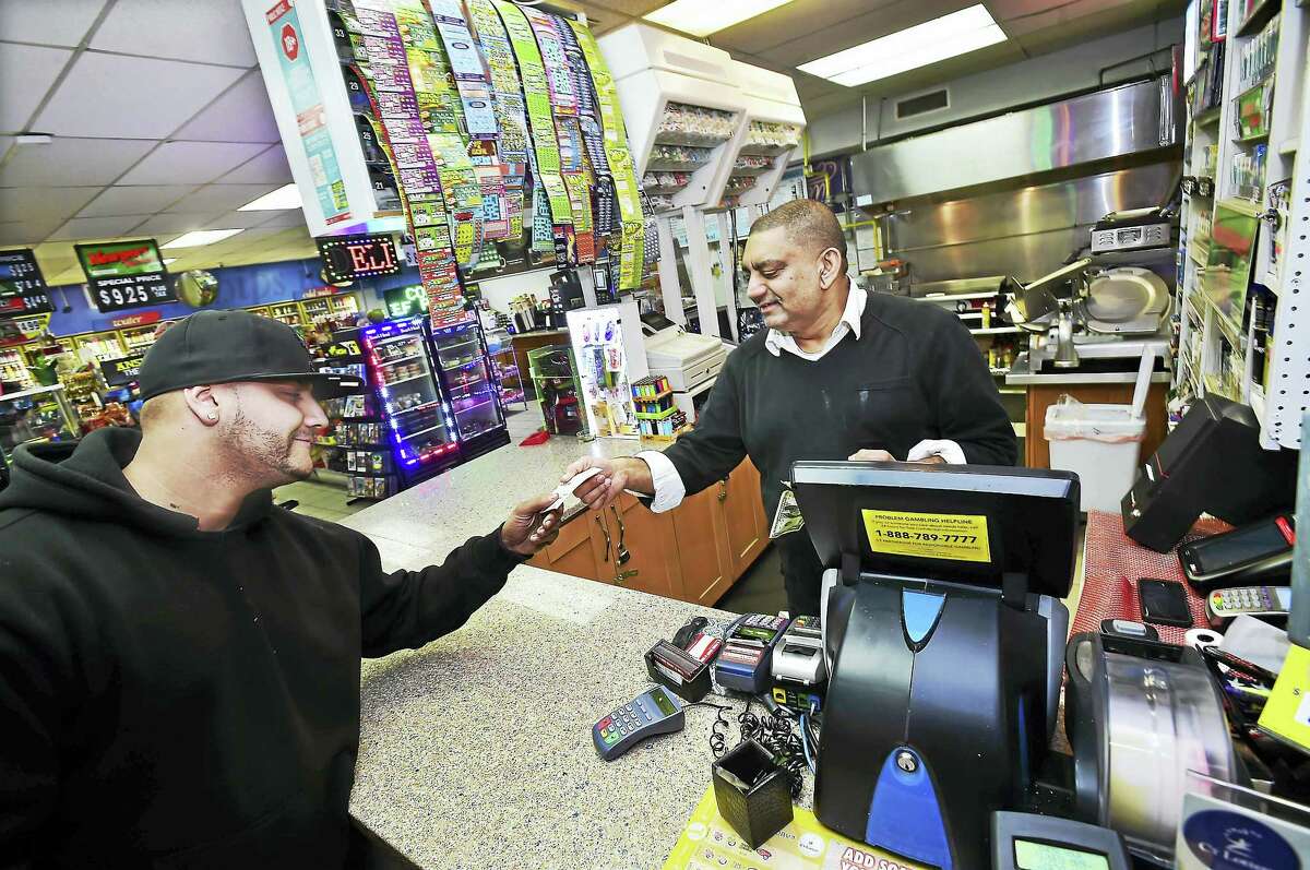 Nick Sarwar, who owns S&B Food Mart & Deli with his wife, Samina Bashir, hands a Powerball ticket to Billy Revis of New Haven Thursday night.