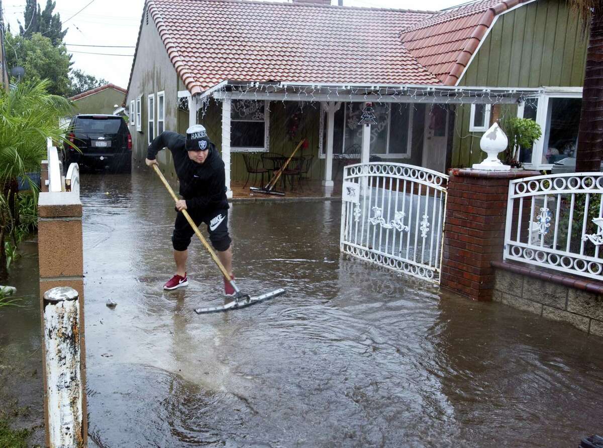 A resident of one of the houses on E. McFadden Avenue in Santa Ana, Calif., squeegees water out of the driveway of the home, Wednesday, Jan. 6, 2016. El Nino storms lined up in the Pacific, promising to drench parts of the West for more than two weeks and increasing fears of mudslides and flash floods in regions stripped bare by wildfires. At least two more storms are expected to follow bringing as much as 3 inches of rain.