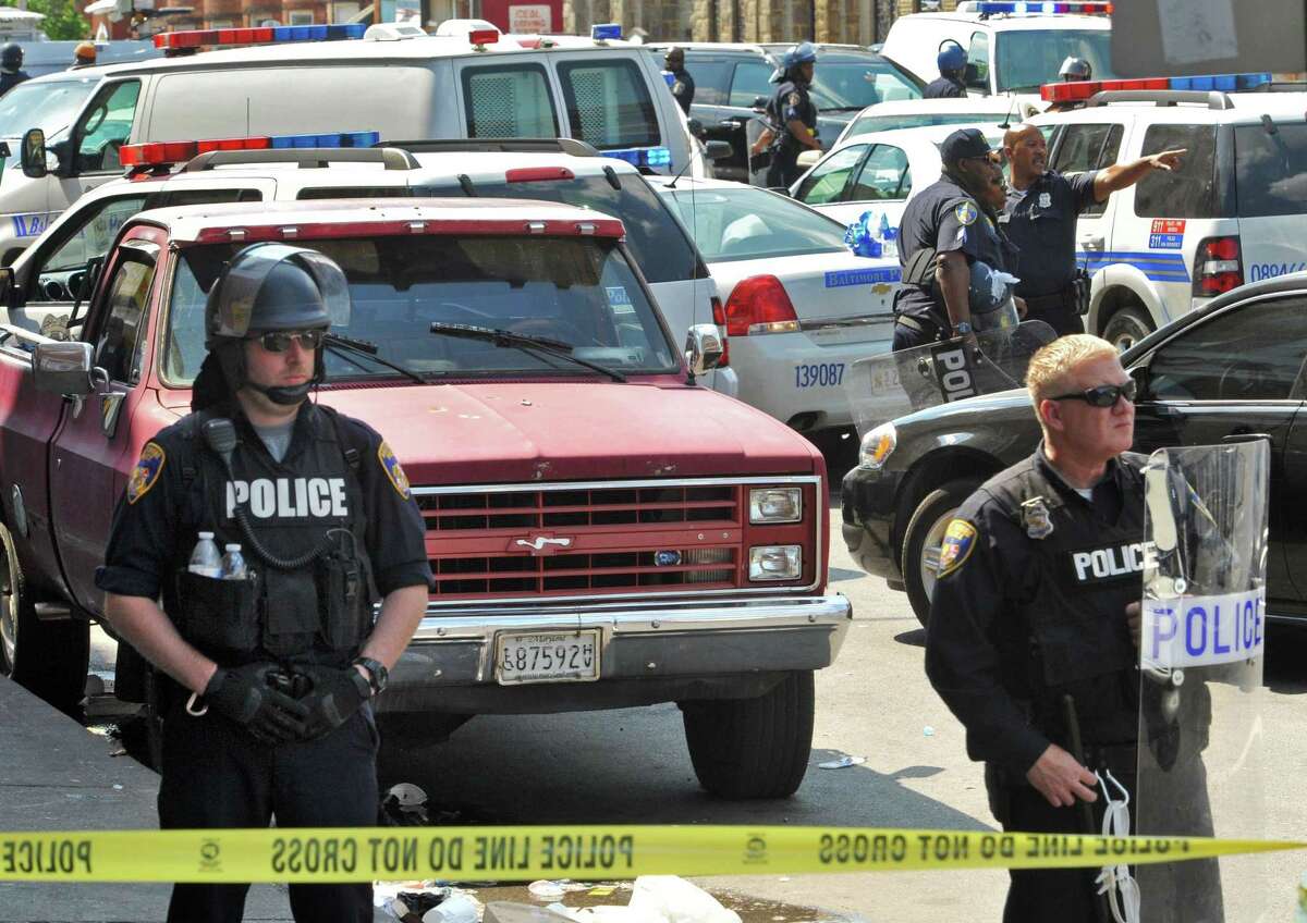 Police stand behind tape Monday, May 4, 2015, in Baltimore. Lt. Col. Melvin Russell said police pursued a man who was spotted on surveillance cameras and appeared to be armed with a handgun. Police said the man was taken into custody after a brief chase, during which a gunshot was heard.