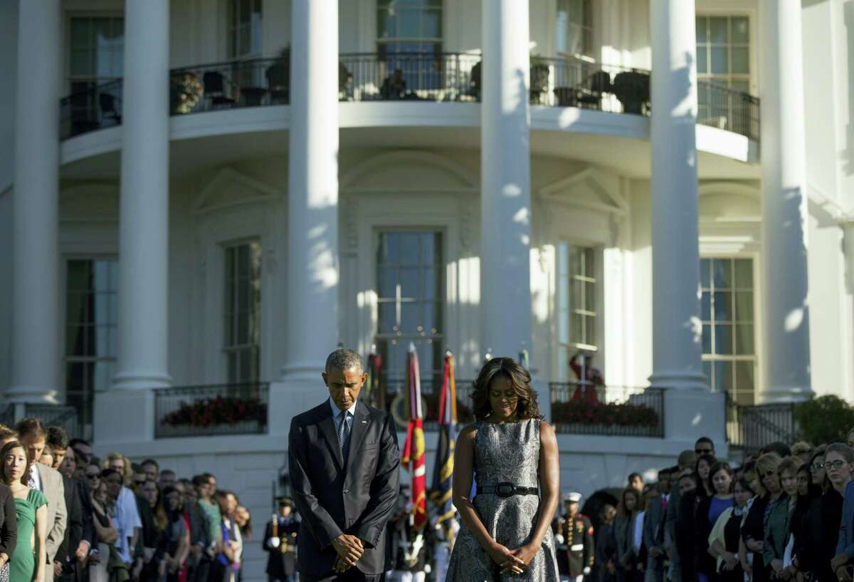 In this Sept. 11, 2015 photo, President Barack Obama, first lady Michelle Obama, and others, pause on the South Lawn of the White House in Washington as they observe a moment of silence to mark the 14th anniversary of the 9/11 attacks. President Barack Obama is joining the nation in remembering the nearly 3,000 people who died in the Sept. 11 attacks 15 years ago Sunday, Sept. 11, 2016.