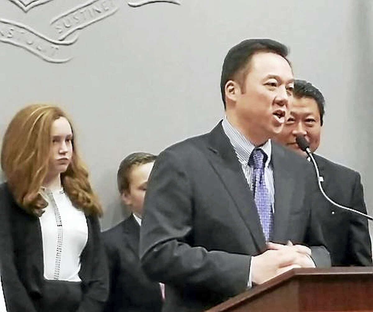 Rep. William Tong speaks to reporters with school children behind him.