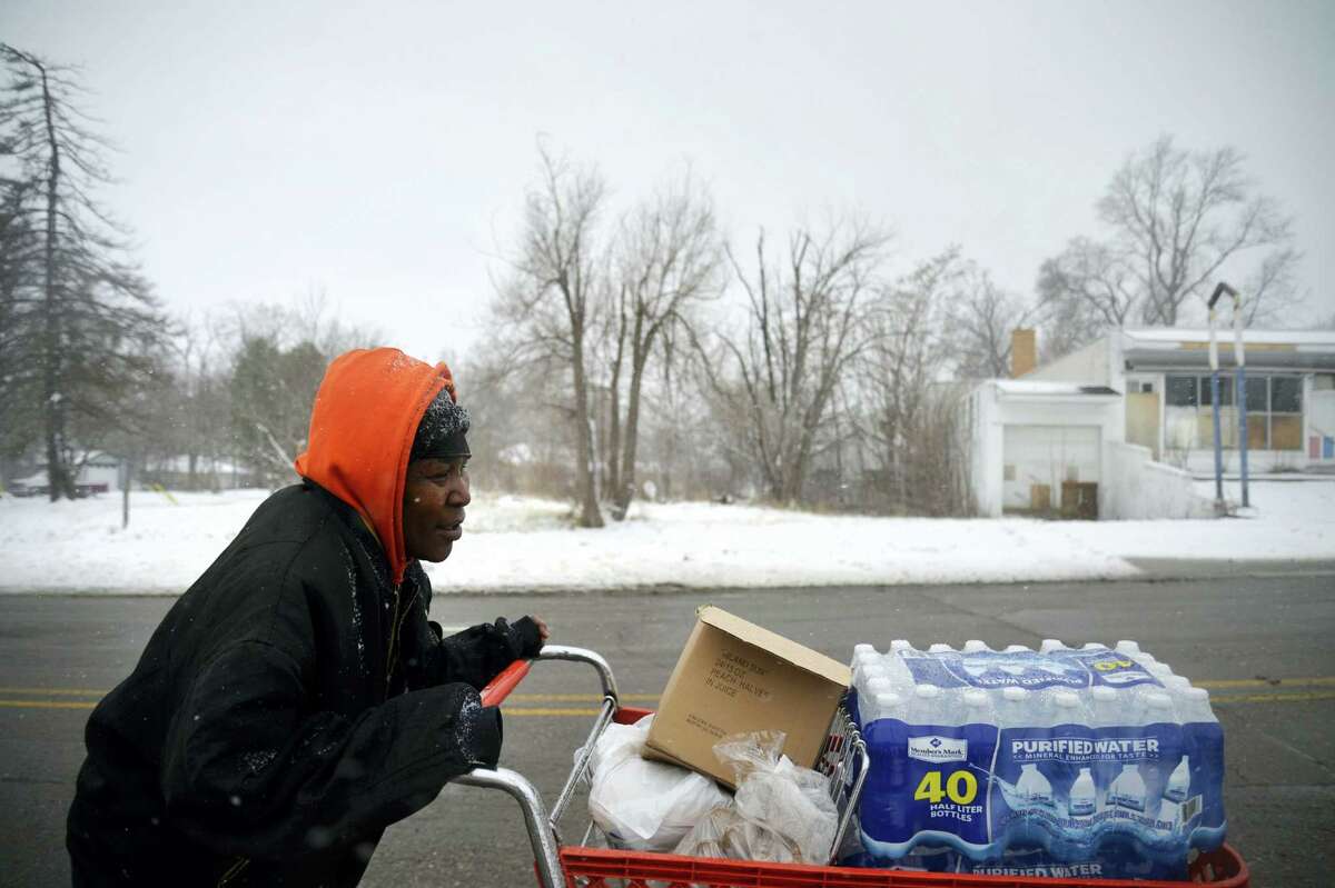 Ulunda Green walks with a cart full of food and water to her home after the first Food Bank food distribution on Wednesday, Feb. 24, 2016, in Flint, Mich. The Food Bank of Eastern Michigan of Flint is partnering with the Michigan Department of Health and Human Services to provide truckloads of food in February and March. Officials say the mobile food pantry will be used in Flint to help increase access to nutritious food that can limit the effects of lead exposure.