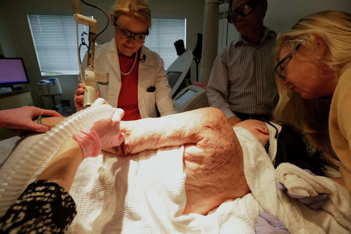 In this Sept. 26, 2015 photo, Dr. Jill Waibel, left, applies a laser to the arm of Kim Phuc to reduce the pain and appearance of her burn scars in Miami. Phuc’s husband, Toan Huy Bui, stands at center with patient care coordinator, Deborah Lomax, right.