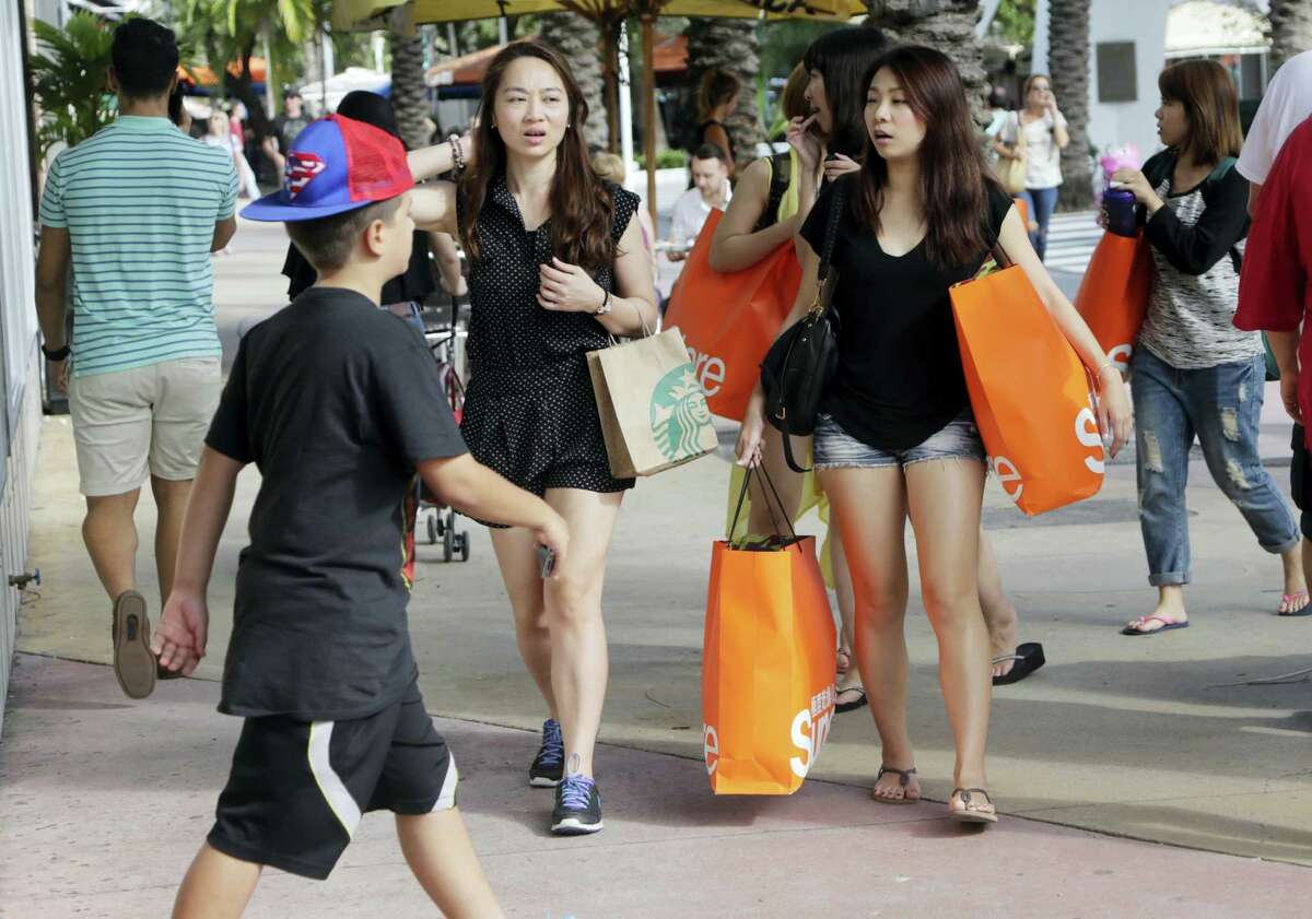 In this Feb. 3, 2016, photo, tourists from Taiwan carry shopping bags as they walk along Lincoln Road Mall, a pedestrian area featuring retail shops and restaurants in Miami Beach, Fla. The Conference Board releases its February index on U.S. consumer confidence on Feb. 23, 2016.