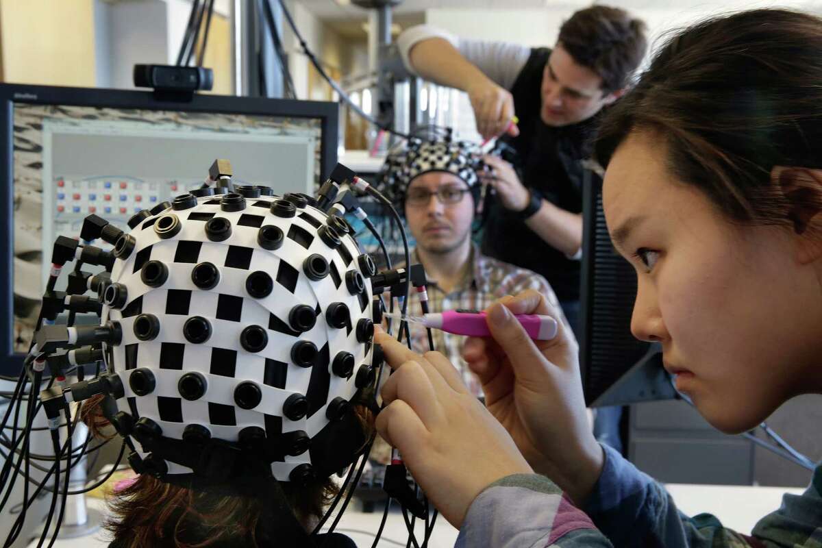Undergraduate student Jenny Park, right, attaches laser probes to Shaw Bronner, as Adam Noah does the same to Shaul Yahil, at the Yale Brain Function Lab during a demonstration of brain mapping technology in New Haven this spring. At one end of each of the 64 fiber optic cables in each headpiece, weak laser beams saw about an inch into their brains to detect blood flow.