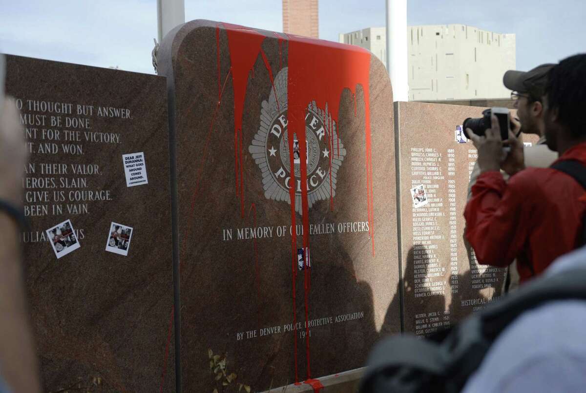 In this photograph taken Saturday, Feb. 14, 2015, protesters take pictures of red paint that was thrown on the memorial to fallen police officers located outside Denver Police headquarters in Denver. More than 100 protesters marched in the streets of Denver to call attention to several recent on-duty police shootings. Protesters defaced the memorial during the march and a decision by Denver Police Chief Robert White to not approach the protesters has triggered counter protests by officers and their supporters. (AP Photo/The Denver Post, Brent Lewis) MAGS OUT; TV OUT; INTERNET OUT; NO SALES; NEW YORK POST OUT; NEW YORK DAILY NEWS OUT
