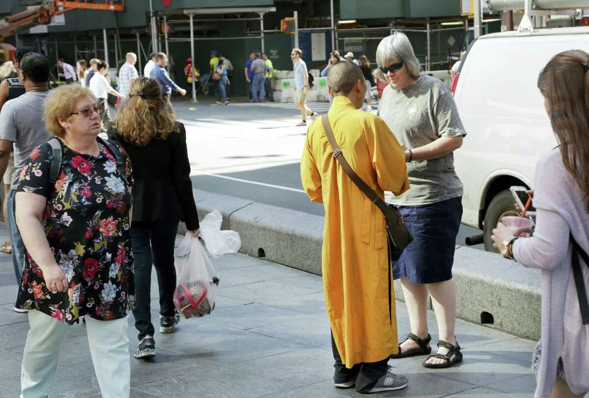 In this Friday, June 24, 2016, photo, a man wearing an orange robe talks with a woman in New York’s Times Square. They wear orange robes and carry shiny medallions, stopping people in New York City to offer greetings of peace. The men identify themselves as Buddhist monks and solicit donations for a temple in Thailand. But the Buddhist Council of New York says the men are ‘Äúfake monks’Äù who are not affiliated with any known temple and are just looking to make a quick buck.