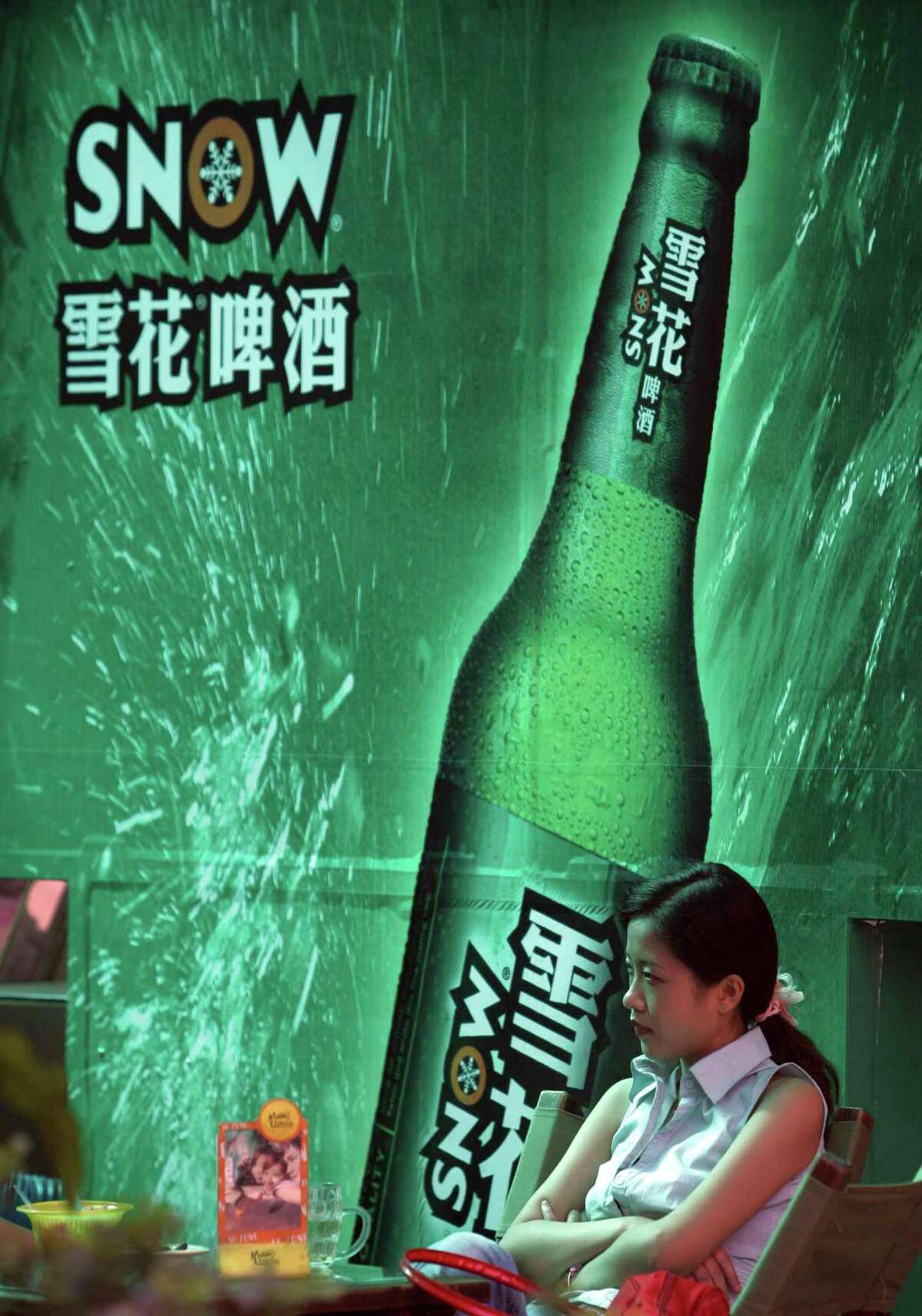 In this Sept. 11, 2006, photo, a woman sits near an advertising poster for Snow Beer in a bar in southwestern China’s Chongqing municipality. A potential prize for AB InBev in its bid for SABMiller is a Chinese beer, Snow, that is the world’s biggest seller. But any deal will face Chinese regulators who have barred the two brewing giants in the past from cooperating.