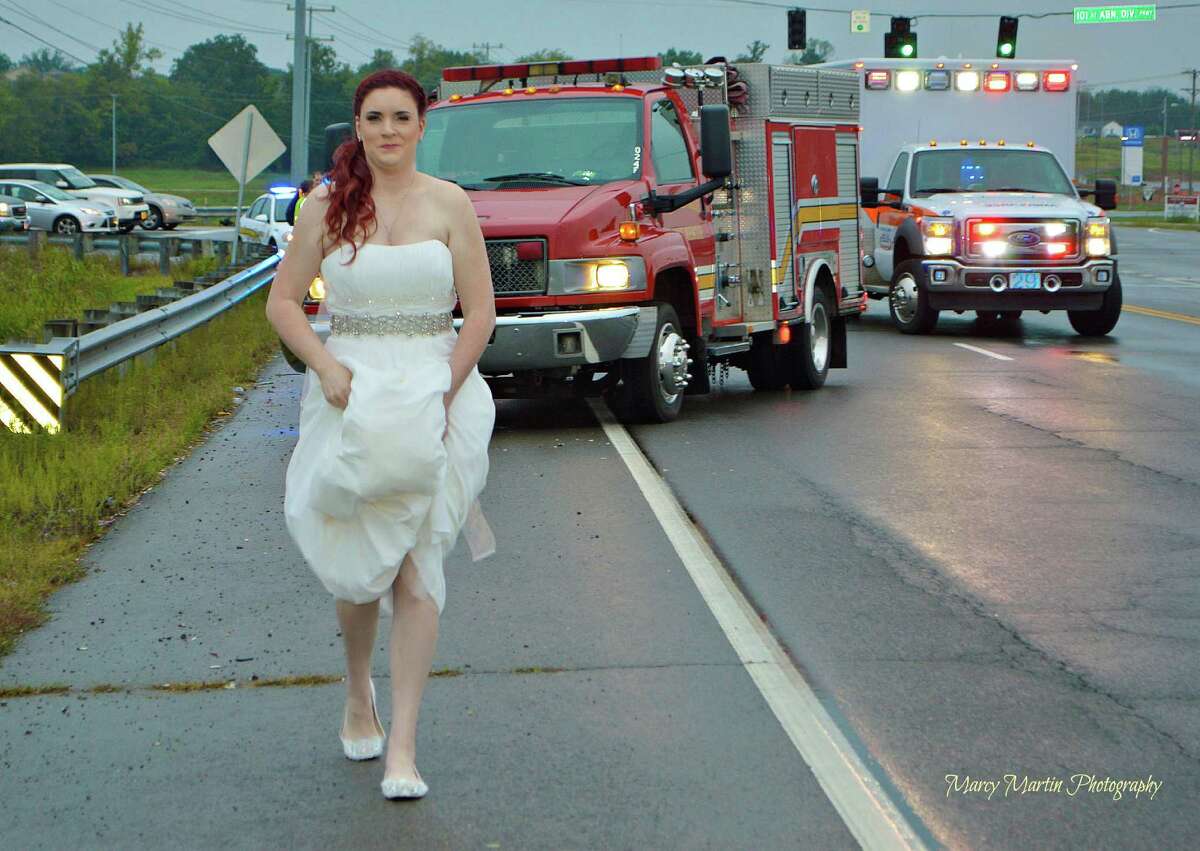 In this Oct. 3, 2015 photo provided by Marcy Martin Photography, her daughter Sarah Ray, in her wedding dress, attends to a car crash in Clarksville, Tenn. Ray’s father and grandparents where in a car crash on their way to Ray’s wedding reception. Ray, who is a paramedic, went to the scene to check on her relatives.