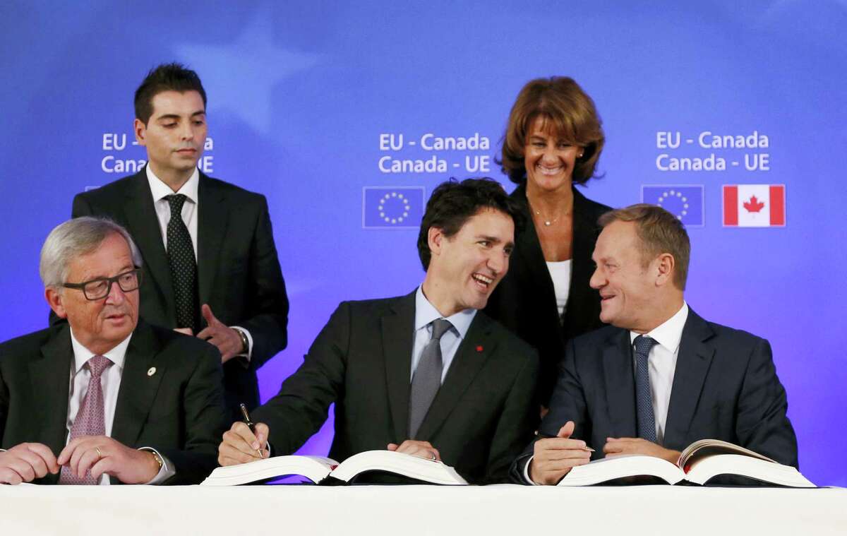 Canadian Prime Minister Justin Trudeau, center front, sits with European Commission President Jean-Claude Juncker, left, and European Council President Donald Tusk, right, as they sign the Comprehensive Economic and Trade Agreement (CETA) during an EU-Canada summit at the European Council building in Brussels on Oct. 30, 2016.