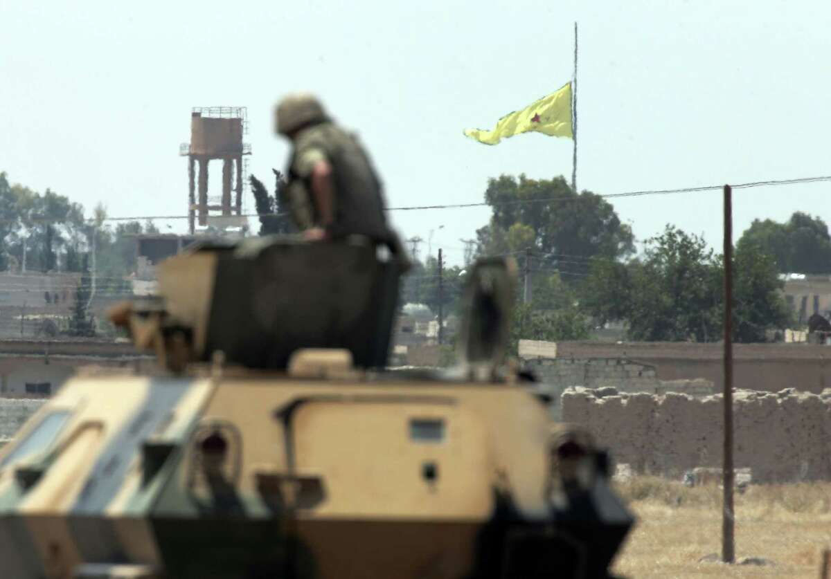 In this photo taken from the Turkish side of the border between Turkey and Syria, in Akcakale, southeastern Turkey, a Turkish soldier on an armoured personnel carrier watches as in the background a flag of the Kurdish People’s Protection Units, or YPG, is raised over the city of Tal Abyad, Syria on June 16, 2015. Kurdish fighters with the YPG, captured large parts of the strategic border town of Tal Abyad from the Islamic State group Monday, dealing a huge blow to the group which lost a key supply line for its nearby de facto capital of Raqqa, a spokesman for the main Kurdish fighting force said.