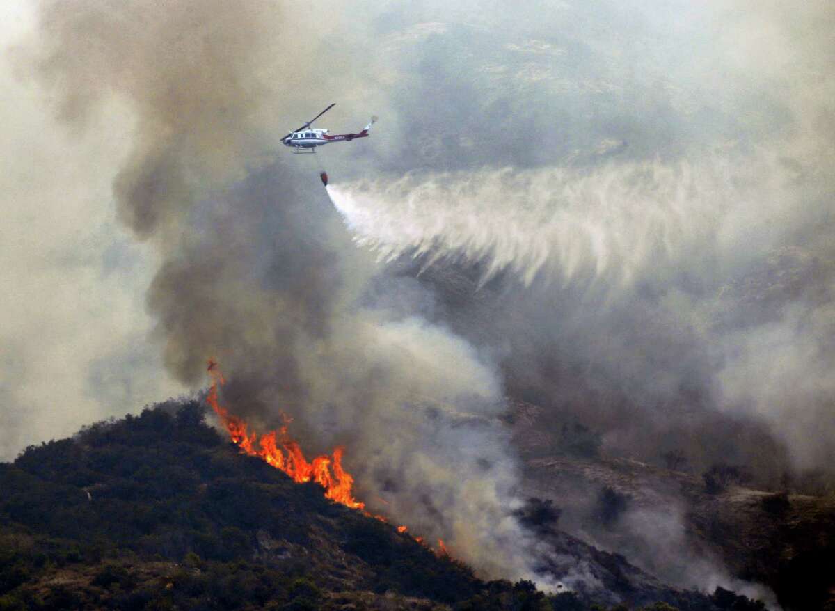 A firefighting helicopter makes a water drop over a wildfire near Bradbury, Calif. on Wednesday, June 22, 2016. Cooler, more humid weather gave at least some temporary help Wednesday to crews battling dangerous wildfires in Southern California, while other blazes across the West were on the move.