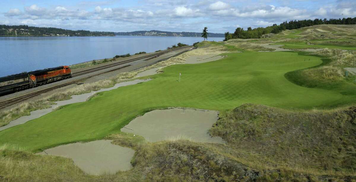 The 16th hole of the Chambers Bay golf course is shown as a freight train passes at left in University Place, Wash.