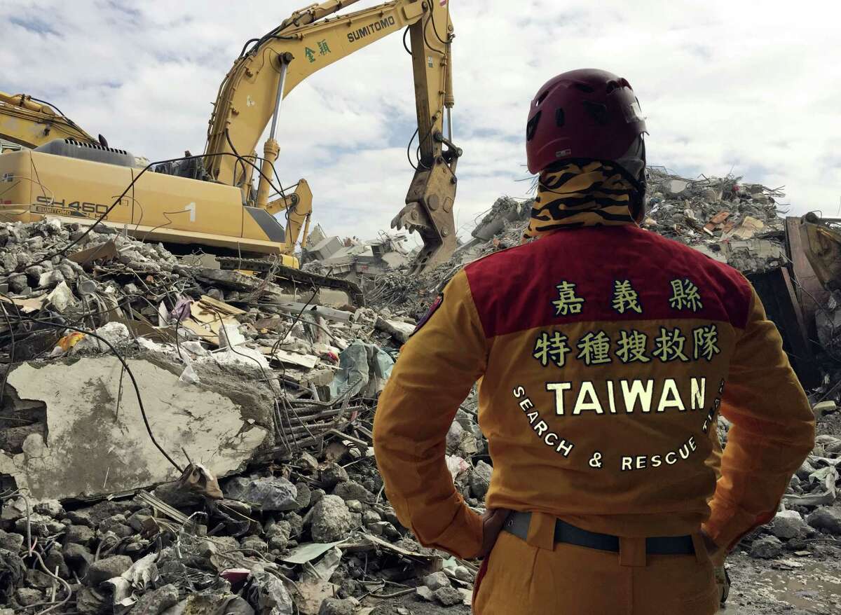 A member of rescue teams stands by Thursday, Feb. 11, 2016, as heavy excavation machinery continues to dig through the rubble of a collapsed building complex in Tainan, Taiwan. The Tainan District Prosecutors Office said in a statement Wednesday that they have approved the detention of three construction company executives who are suspected to have overseen shoddy construction of the 17-story Weiguan Golden Dragon building, which tumbled on to its side following an earthquake Feb. 6. Rescue efforts have now ended, Taiwan authorities said Saturday.