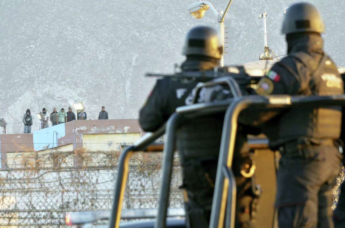 Inmates stand on the rooftop of the Topo Chico prison as police stand guard on the perimeters, after a riot broke out around midnight, in Monterrey, Mexico, Thursday, Feb. 11, 2016. Dozens of inmates were killed and several injured in a brutal fight between two rival factions at the prison in northern Mexico, the state governor said.