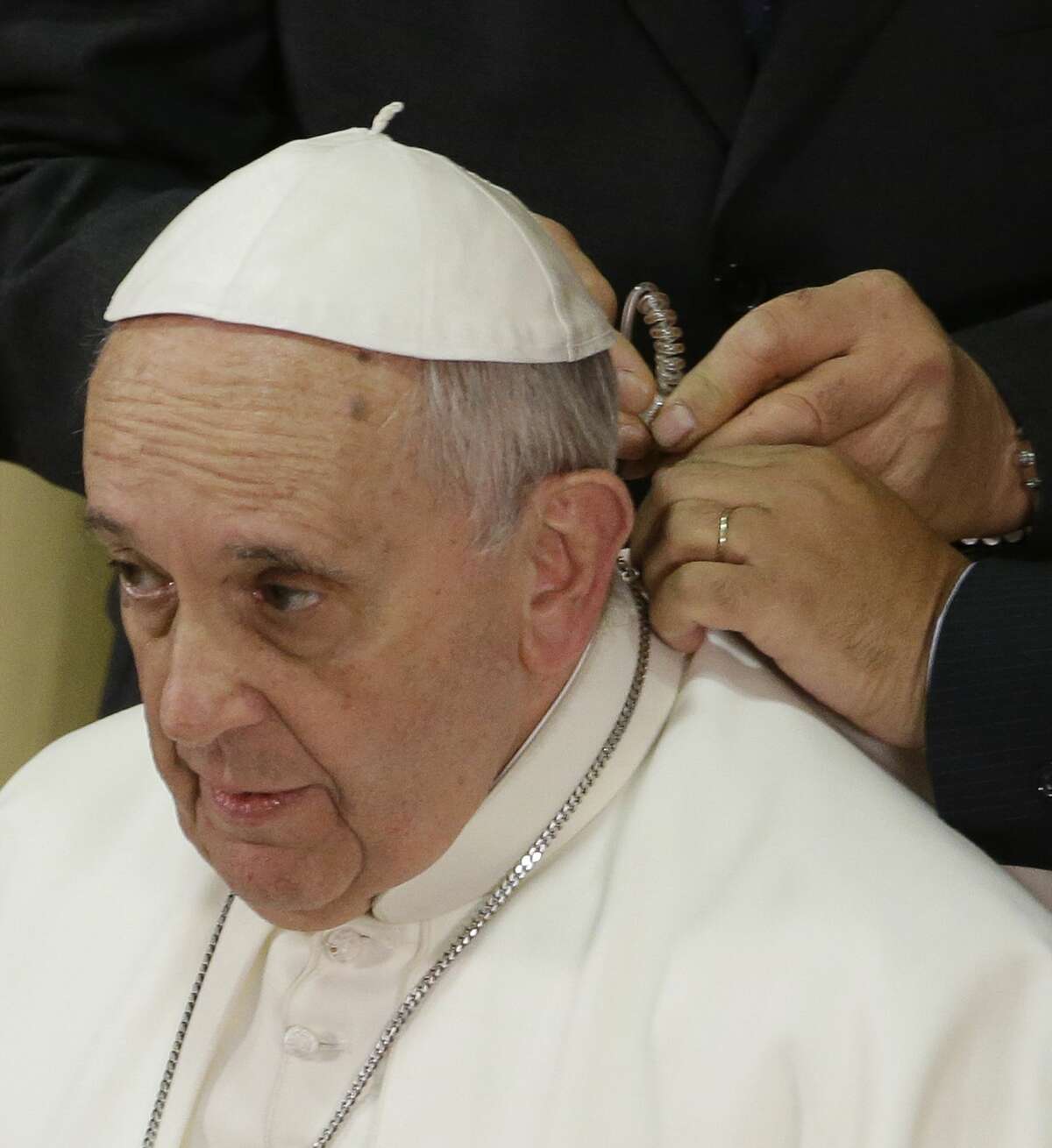 Pope Francis has an headset applied by two Vatican radio technicians prior to giving his his speech in the Synod hall on the occasion of the closing ceremony of the IV Scholas Occurrentes World Educational Congress, at the Vatican, Thursday, Feb. 5, 2015. (AP Photo/Gregorio Borgia)
