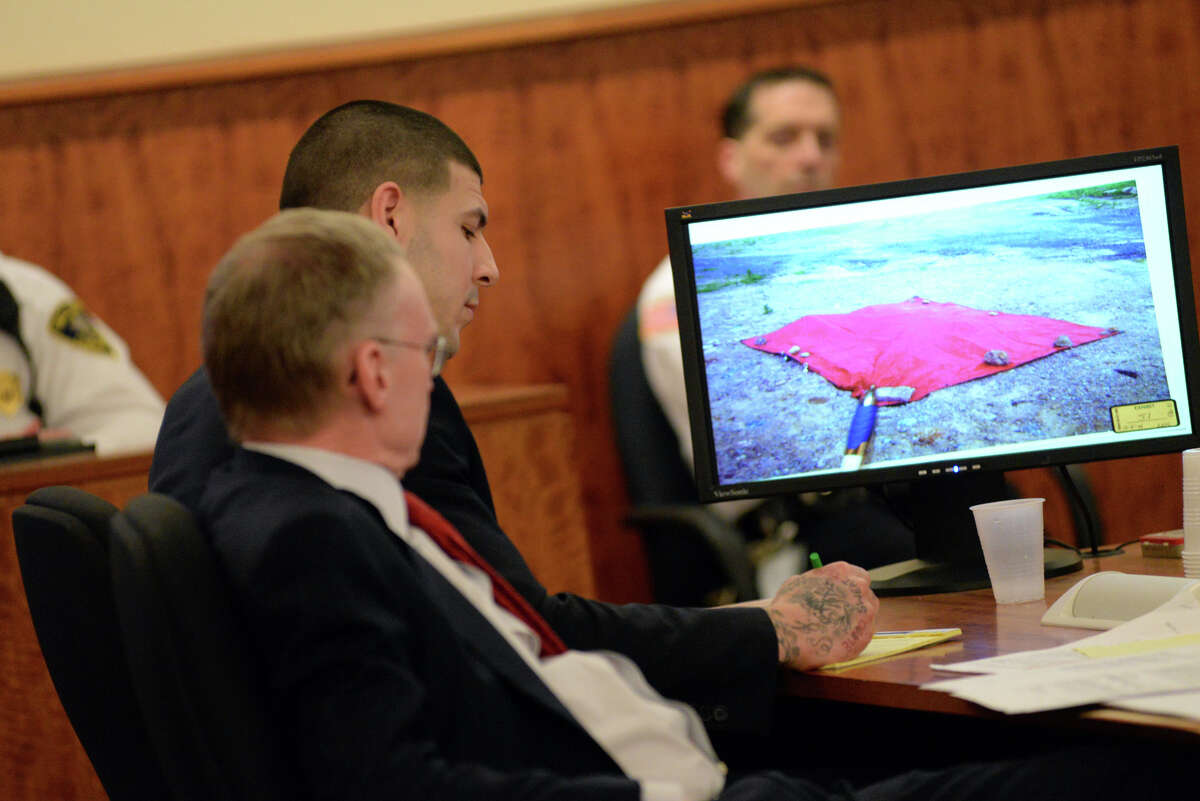 Former New England Patriot Aaron Hernandez takes notes next to his attorney, Charles Rankin, as a photo of the covered body of Odin Lloyd is displayed on a screen during his murder trial Thursday at Bristol County Superior Court in Fall River, Mass.