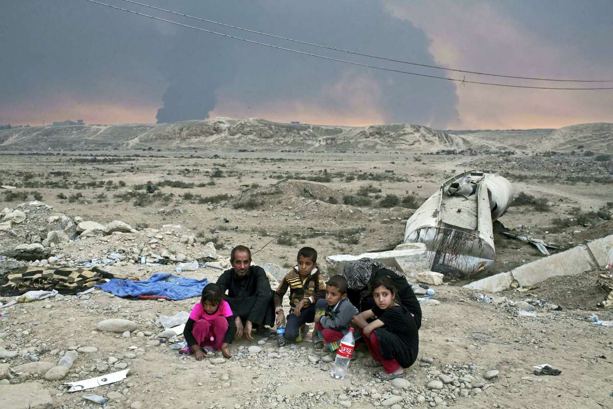 Internally displaced persons sit at a checkpoint as smoke rises from the burning oil wells in Qayyarah, about 31 miles (50 km) south of Mosul, Iraq on Oct. 23, 2016. Islamic State fighters torched a sulfur plant south of Mosul, sending a cloud of toxic fumes into the air that mingled with oil wells the militants had lit on fire to create a smoke screen.