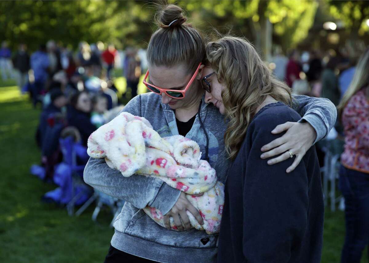 Ashley Katter, left, embraces Haley Lamphere while holding Katter’s niece Ruby Abrahamson during a prayer vigil Saturday, Oct. 3, 2015, in Winston, Ore. The vigil was held in honor of the victims of the fatal shooting at Umpqua Community College on Thursday.