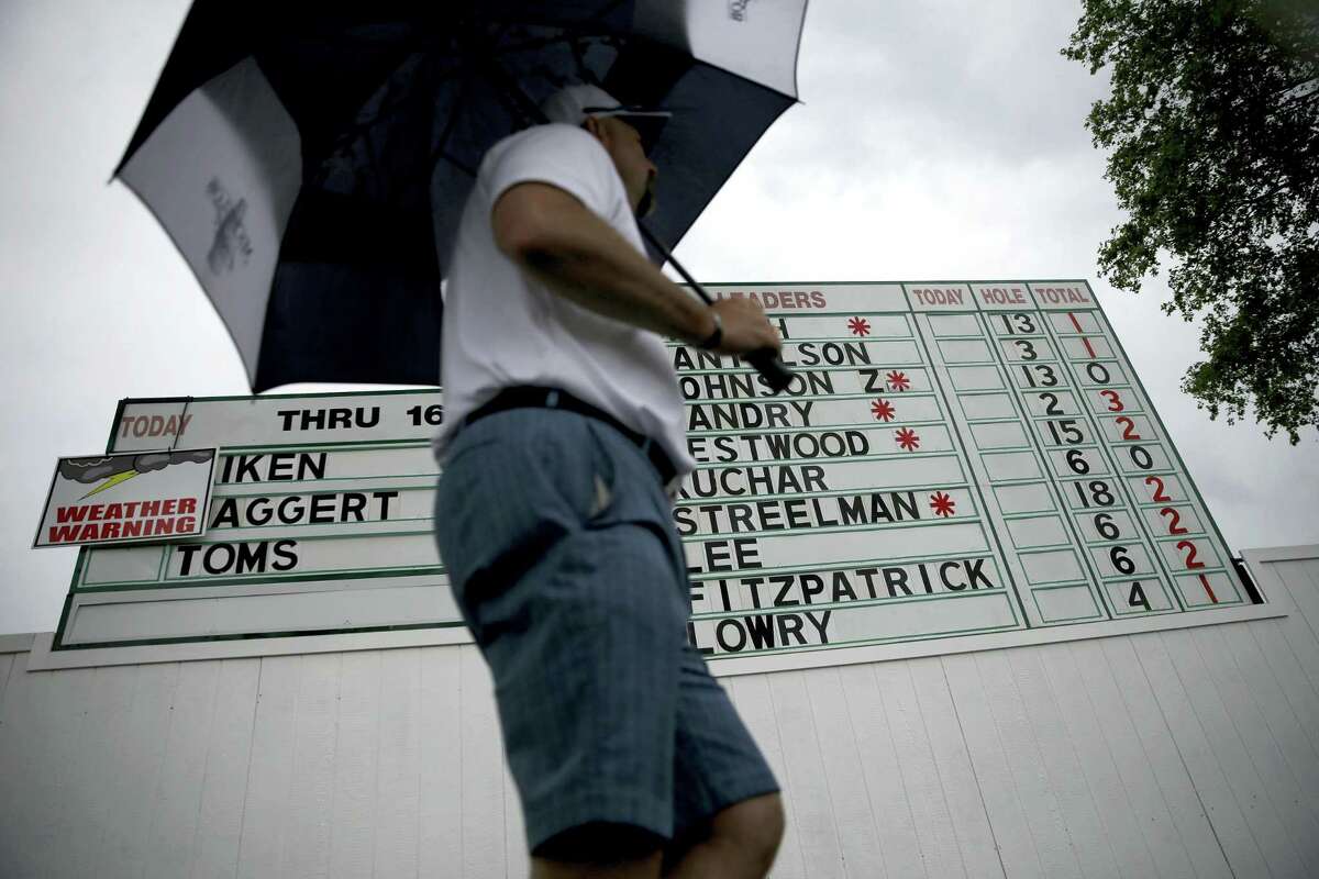 A fan with an umbrella walks past the leaderboard during a rain delay during the first round of the U.S. Open on Thursday.