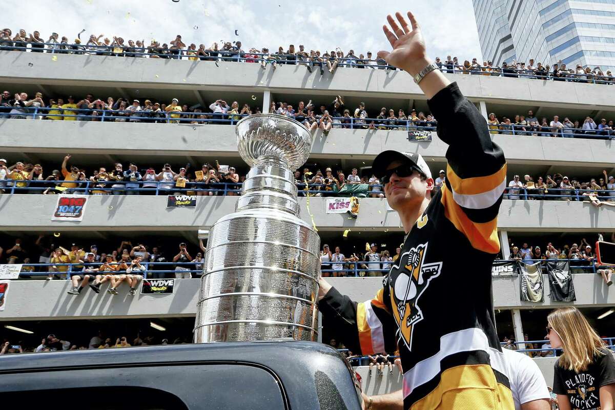 Pittsburgh Penguins’ Sidney Crosby waves to the crowd while holding onto the Stanley Cup while riding along the victory parade route in Pittsburgh, Pa., Wednesday.