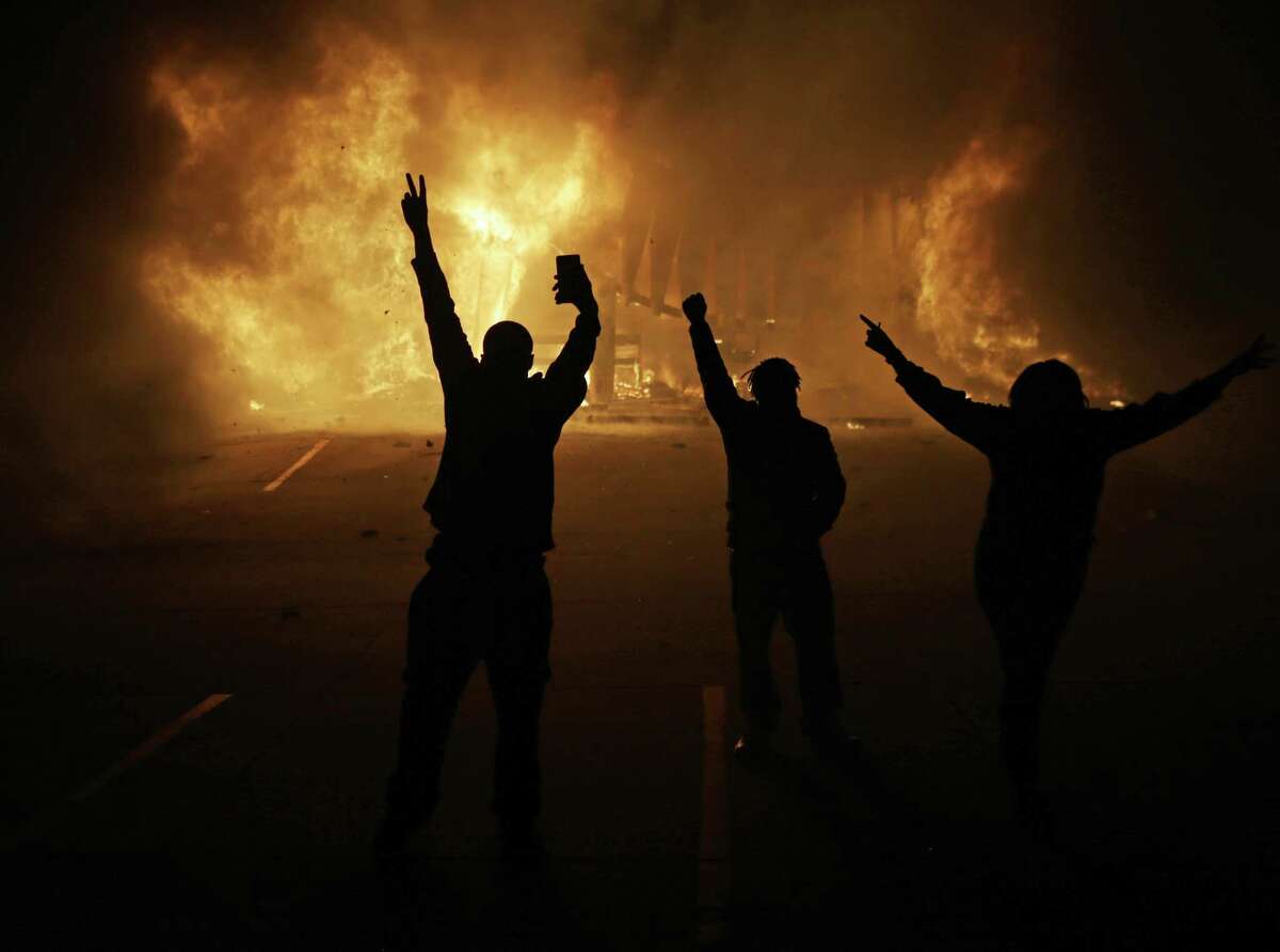 In this Nov. 25, 2014, file photo, people watch as stores burn in Ferguson, Mo., after a grand jury decided not to indict Ferguson police Officer Darren Wilson in the death of Michael Brown, the unarmed, black 18-year-old whose fatal shooting sparked sometimes violent protests. The U.S. Department of Justice on Friday, Oct. 2, 2015, will release the findings of the last of its third and final review stemming from the unrest in Ferguson.