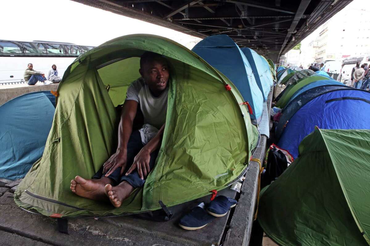 In this photo taken Monday, May 25, 2015, Mandela Drame, from Ivory Coast, speaks with The Associated Press as he sits in his tent placed alongside dozens of others set up by migrants under a metro bridge near the Gare du Nord station in Paris, France. Hundreds of migrants, mostly from east Africa, have poured into the ersatz tent camp on the bridge under a rumbling subway line and over tracks that take Eurostar trains to Britain. (AP Photo/Remy de la Mauviniere)