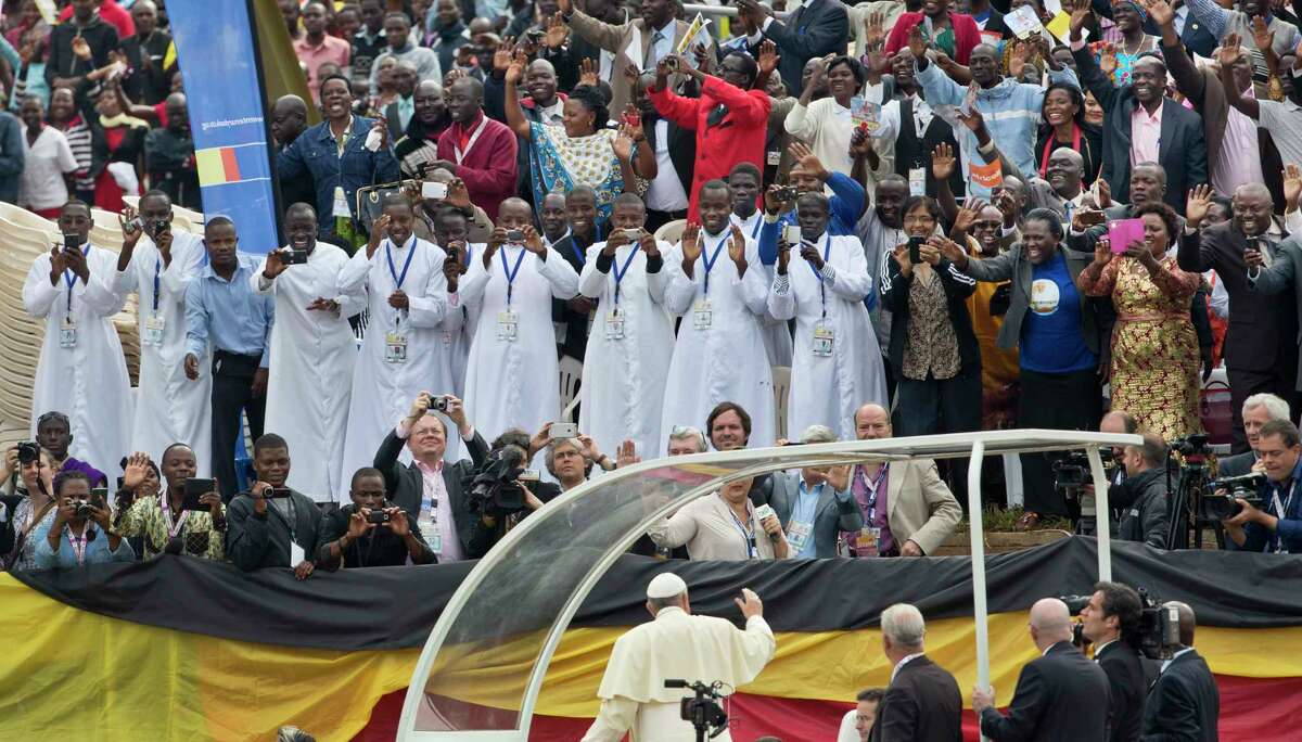 Members of the audience cheer and take photographs with their smartphones as Pope Francis, below, drives around the venue before leading a Holy Mass for the Martyrs of Uganda at the area of the Catholic Sanctuary in the Namugongo area of Kampala, Uganda Saturday, Nov. 28, 2015. Pope Francis is in Uganda on his first-ever trip to Africa, a six-day pilgrimage that has already taken him to Kenya and then onwards to the Central African Republic.