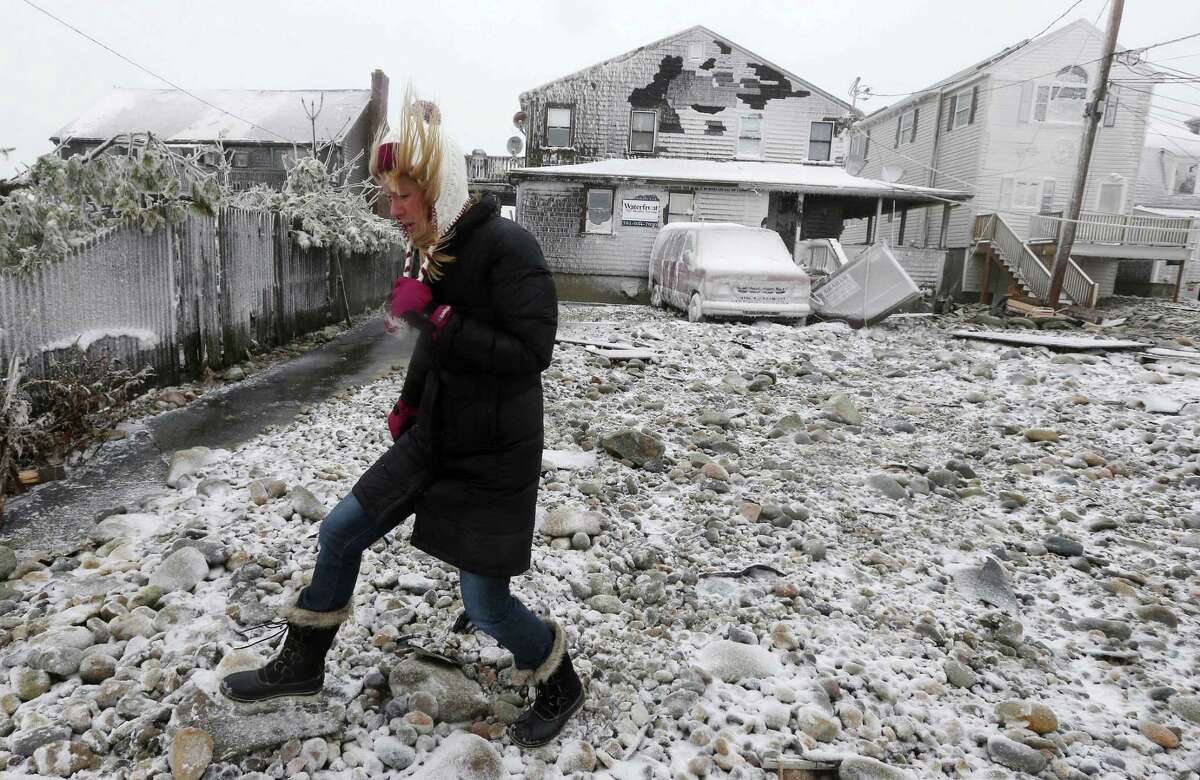 FILE - In this Tuesday, Jan. 27, 2015 file photo, Lynn Leary walks past houses damaged by ocean waves during a winter storm in Marshfield, Mass. New Englandís epic winter is on pace to produce an epic number of insurance claims. Thousands of homeowners are filing claims as they begin to repair the damage brought by an especially brutal winter. (AP Photo/Michael Dwyer, File)