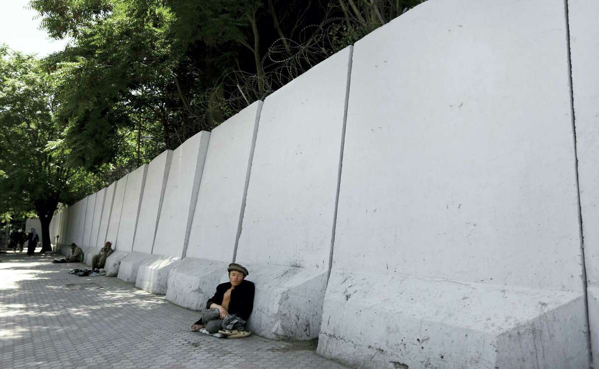 In this Wednesday, May 25, 2016, photo, an Afghan bigger sits in front of blast walls installed to cordon off the Ministry of Communications in Kabul, Afghanistan. With every terrorist attack in Kabul, a little more of what made Afghanistan’s capital a garden city of the 1960s disappears behind massive concrete walls designed to thwart suicide bombers and keep the people and buildings behind them safe.