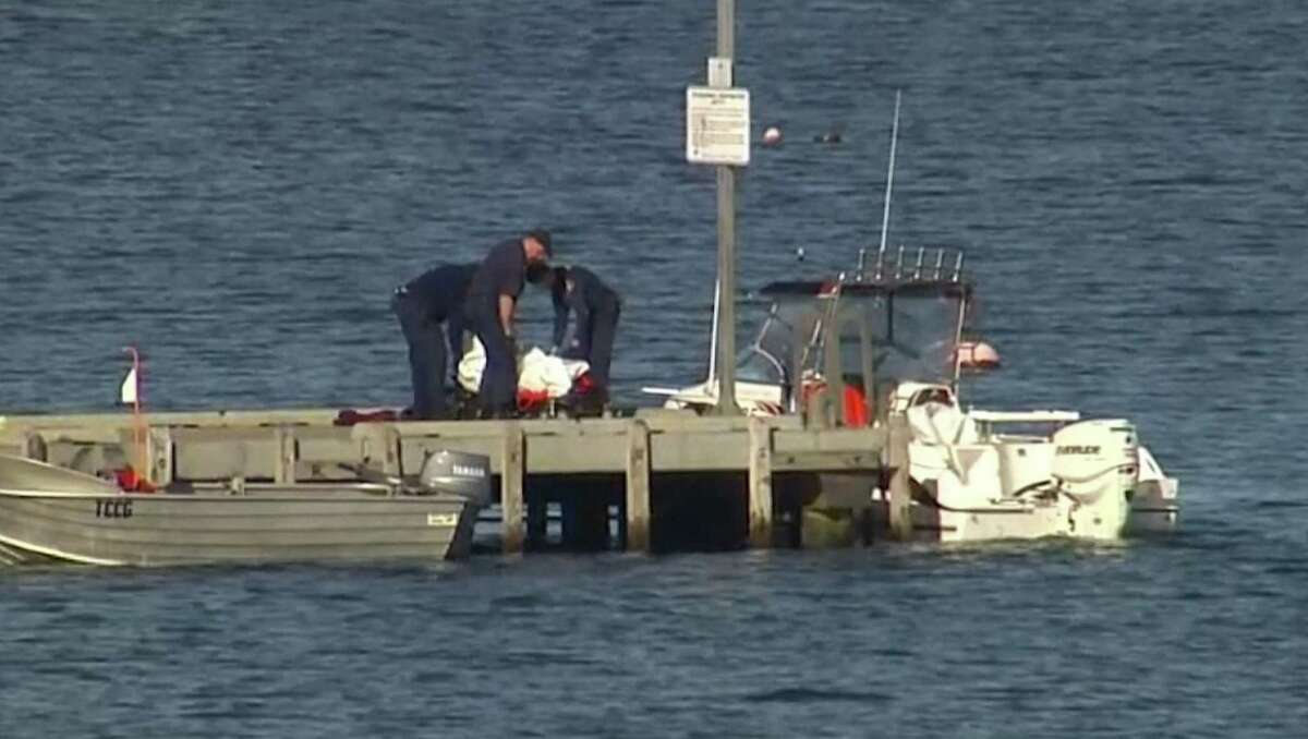 In this image taken from video, police carry a body in a bag and place it in on a stretcher on a jetty in Triabunna, off the Australian island state of Tasmania, on Saturday, July 25, 2015. A woman watched her father being mauled to death by a large shark on Saturday while the pair were diving, police said.